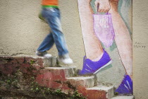 Person walkjing down stone steps past mural of feet walking up stairs.