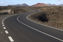 Distant view of Timanfaya National Park and the Montanas del Fuego from scenic west coast road following bend in foreground.volcanic Espainia Espana Espanha Espanya European Hispanic Southern Europe...