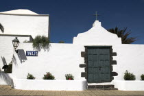 Tinajo village in island interior.  Section of white painted walls of village church with green painted door  plants and lantern casting strong shadow on wall.Espainia Espana Espanha Espanya European...