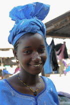 Tanji Village.  Head and shoulders portrait of smiling African girl with a gold tooth and wearing blue dress and traditional tied head scarf in bright sunshine. TanjehTanjihsmilewomancolourcolor...