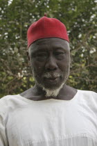 Tanji Village.  Head and shoulders portrait of Muslim man with white trimmed beard wearing white shirt and red cap.TanjehTanjih  AfricanfaceexpressioncharacteristicsemotionmoodraceethnicIsl...