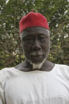 Tanji Village.  Head and shoulders portrait of Muslim man with white trimmed beard wearing white shirt and red cap.TanjehTanjih  AfricanfaceexpressioncharacteristicsemotionmoodraceethnicIsl...