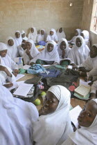 Tanji Village.  African Muslim girls wearing white headscarves while attending a class at the Ousman Bun Afan Islamic school sitting in groups around desks with bags and books piled in centre.Tanjeh...