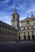 Exterior facade of San Lorenzo El Escorial palace and monastery complex with visitors standing in square in the foreground.
