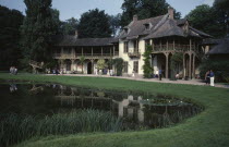 Versailles.  The Queens Cottage in the Hamlet  exterior with tourist visitors reflected in pond.
