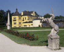 Hellbrunn Palace  yellow building seen from across gardens with a unicorn statue in the foreground