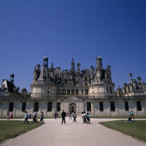 Chambord Chateau. Tourists on gravelled entrance between green lawns. Blue sky