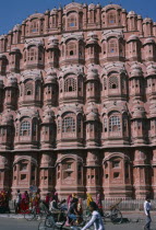 Hawa Mahal or Palace of the Winds.  Part view of semi-octagonal  honeycombed sandstone facade.   Cyclists and brightly dressed women on street in front.