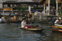 Woman rowing canoe containing flowers with woman on the jetty behind loading boat with wicker baskets.