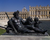 Versailles . Part view of palace behind bronze reclined statue of man with child next to pond