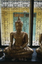 Seated Buddha covered with gold leaf in front of window with decorative metal shutter.Asian Prathet Thai Raja Anachakra Thai Religion Siam Southeast Asia Religious Siamese