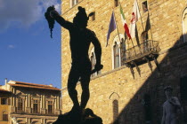 Piazza della Signoria.  Statue of Perseus holding the head of Medusa by Cellini silhouetted against Palazzo Vecchio in sunlight.