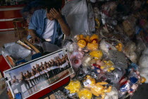 Chinatown. Shop with plastic wrapped toys for sale and picture commemorating the capture of a huge fish by the American Army in 1973.  Male vendor reading behind.Asian Prathet Thai Raja Anachakra Tha...