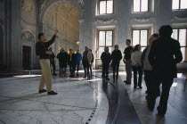 Visitors in the Citizens Hall of the Royal Palace  with tour guide standing on a map of the Old World tiled on the floor.