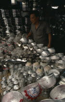 Stall selling chrome / silver kitchen utensils at the weekend market with vendor standing behind.Prathet Thai Raja Anachakra Thai Siam Southeast Asia Asian Siamese