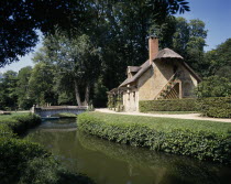 Versalilles Hameau de Trianon. View over river towards thatched cottage.