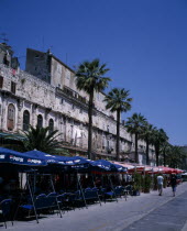 The restored walls of the Diocletian Palace with umbrella coverred cafe tables on the pavement