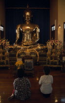 Wat Traimit Temple of The Golden Buddha with two women kneeling at prayer in front of the BuddhaAsian Prathet Thai Raja Anachakra Thai Religion Siam Southeast Asia 2 Female Woman Girl Lady Religious...