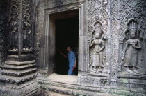 Ta Prohm.  Woman visitor framed in doorway of twelth century Buddhist temple with exterior wall decorated with bas relief carvings of apsaras.Asian Cambodian Kampuchea Religion Southeast Asia Female Women Girl Lady History Holidaymakers Kamphuchea Religion Religious Buddhism Buddhists Tourism Tourist Female Woman Girl Lady Sightseeing Tourists