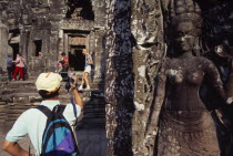 The Bayon.  Tourists with cameras and videos with bas relief carving of apsara in the foreground.Asian Cambodian Kampuchea Religion Southeast Asia History Holidaymakers Kamphuchea Religious Tourism