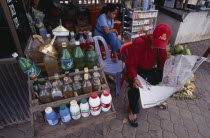Roadside stall selling bottles of petrol watered down and at the same price as at fuel stations. Man sitting reading a newspaperGasoline Asian Cambodian Kampuchea Southeast Asia Kamphuchea Male Men G...