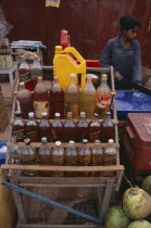 Roadside stall selling bottles of petrol watered down and at the same price as at fuel stations. Woman cutting ice in the backgroundGasoline Asian Cambodian Kampuchea Southeast Asia Female Women Girl...