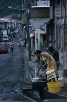 St Lucia, Soufriere, man and woman collecting water from standpipe in narrow street with open gutter.