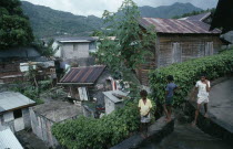 St Lucia, Soufriere, wood and breeze block housing with corrugated tin rooves  hanging washing and children standing on  drainage channel in foreground.