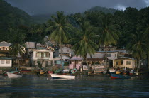 St Lucia, Soufriere, coastal housing and palm trees with colourful boats pulled up along shore,  stormy and overcast sky above.
