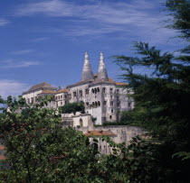 The Royal Palace. Palacio Nacional de Sintra. Conical chimneys rising above palace seen through trees against a blue sky