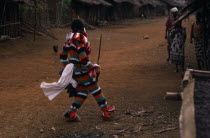 Masked Ju-ju man wearing striped costume taking part in Leopard Cult or Ekpe masquerade in rainforest village near Mundemba. African Cameroonian Central Africa Male Men Guy One individual Solo Lone S...