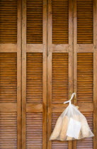 Plastic bag containing loaves of fresh bread tied to the handle of wooden louvre shutter doors