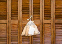 Plastic bag containing loaves of fresh bread tied to the handle of wooden louvre shutter doors