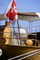 The dome of the Carmelite Church of 1573 seen through the foredeck of an old schooner with a Maltese Cross flag moored on Sliema waterfront