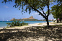 Pigeon Island National Historic Park seen through trees from a nearby beach on a causeway to the island with yachts at anchor in Rodney Bay