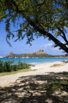 Pigeon Island National Historic Park seen through trees from a nearby beach on a causeway to the island with yachts at anchor in Rodney Bay