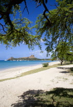 Pigeon Island National Historic Park seen through trees from a nearby beach on a causeway to the island with yachts at anchor in Rodney Bay