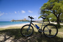 Pigeon Island National Historic Park seen from a nearby beach on a causeway to the island with yachts at anchor in Rodney Bay and a parked mountain bike in the foreground