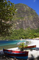 Val des Pitons The white sand beach at the Jalousie Plantation Resort Hotel with the volcanic plug of Petit Piton beyond and tourists on sunbeds beneath palapa sun shades with colourful fishing boats...