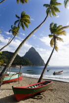 Fishing boats on the beach lined with coconut palm trees with the town and the volcanic plug mountain of Petit Piton beyond