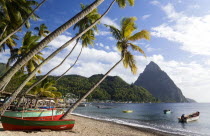 Fishing boats on the beach lined with coconut palm trees with the town and the volcanic plug mountain of Petit Piton beyondCaribbean West Indies Windward Islands Beaches Resort Sand Sandy Scenic Seas...