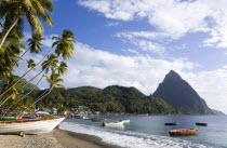 Fishing boats on the beach lined with coconut palm trees with the town and the volcanic plug mountain of Petit Piton beyond. A fishing boat in the foreground with the words Help Me Lord written on the...