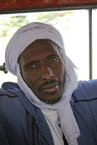 Head and shoulders portrait of African Muslim man travelling on a bus wearing white head-dress and looking direct to camera. faceexpressioncharacteristicsIslamraceGambian Islamic Male Men Guy Mo...
