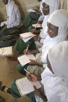 Tanji Village.  African Muslim girls wearing white headscarves while attending a class at the Ousman Bun Afan Islamic school  sitting in line writing in exercise books.TanjihTanjehIslammoslimhead...
