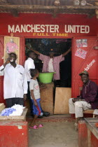 Shop in Gambias capital Banjul painted red and white  the colours of the Manchester United football strip and decorated with slogans and posters with group of African supporters of the team gathered o...