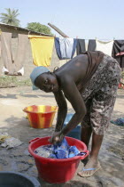 Young woman bending to wash her familys clothes in a bowl before hanging them outside to dry in the yard of their house.TanjehTanjihhouseholddaily lifecleaningcleandryingchoresAfrican Cleans...