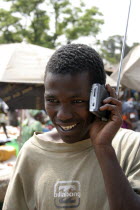 Albert Market  Russell Street.  Young African man smiling  while listening to a radio which he is holding next to his ear.urban lifehappyreceptiosoundreceptionraceContented Gambian Immature Mal...