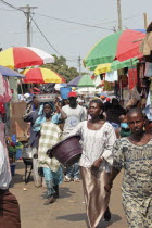 Bakau Market  Atlantic Road.  Busy market scene with crowds of people  and roadside stalls beneath colourful striped sun umbrellas. SerecundaSerekuntaSerecuntaSerekudaAfricanColorful Gambian Wes...