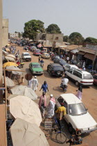 Bakau Market   Atlantic Road.  Main city road lined with street stalls beneath sun umbrellas and open fronted shops with people and cars. SerecundaSerekuntaSerecuntaSerekudaAfricanAutomobiles Au...
