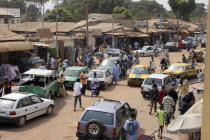 Bakau Market  Atlantic Road.  View of Serekundas main city street lined with open fronted shops and roadside stalls beneath sun umbrellas  people and vehicles. SerecundaSerekuntaSerecuntaSerekuda...